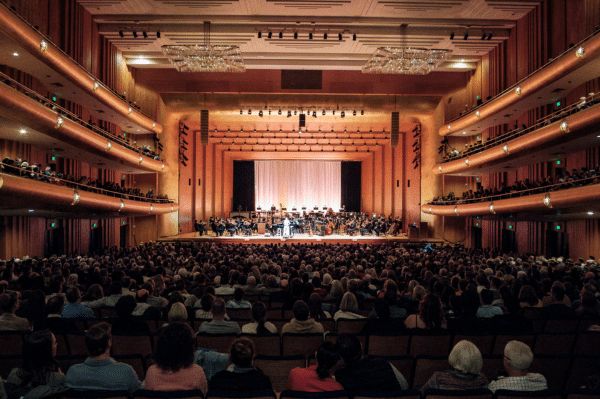 A full concert hall audience watching an orchestra perform on stage.